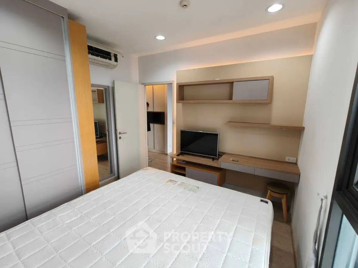 Modern bedroom with built-in wardrobe and TV, featuring sleek design and ample natural light.