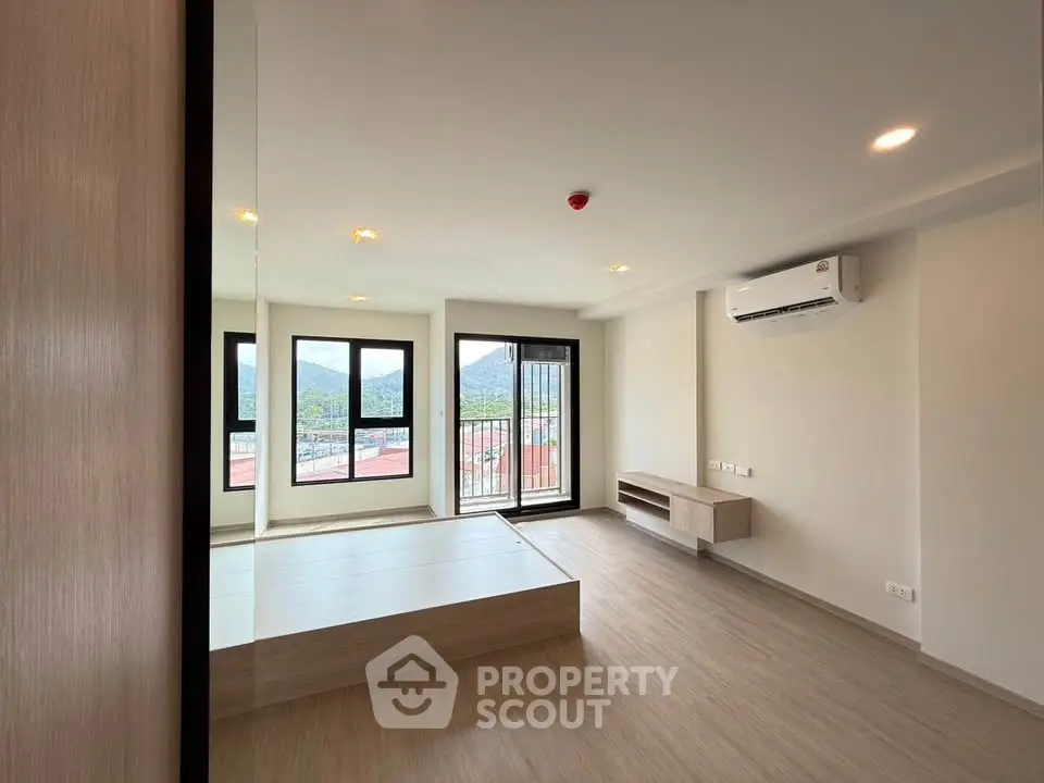 Modern living room with large windows and mountain view, featuring built-in air conditioning and wooden flooring.
