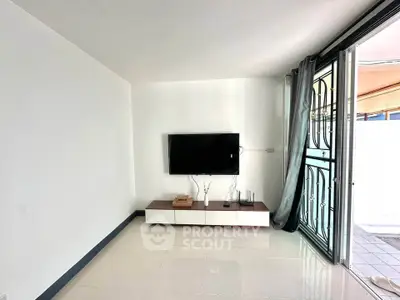 Modern living room with wall-mounted TV and sliding glass doors leading to patio.