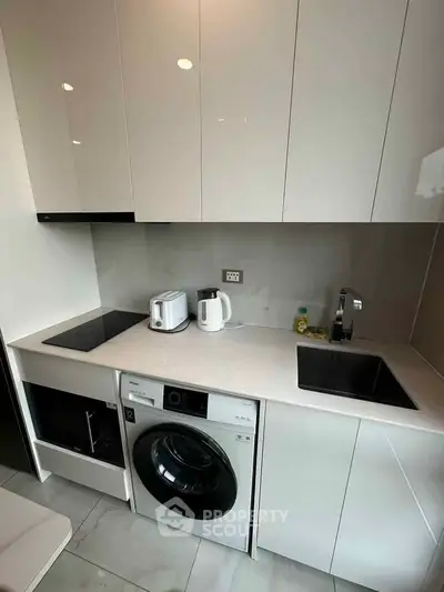 Modern compact kitchen with sleek cabinetry and built-in appliances, featuring a washing machine and electric stove.