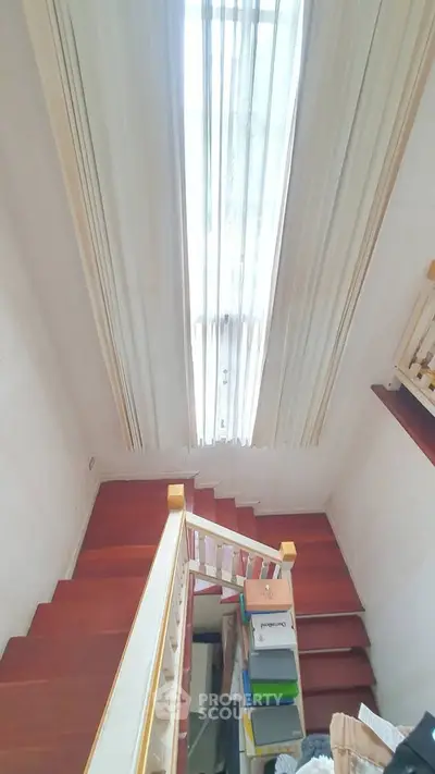 Elegant staircase with wooden steps and tall window drapes in a bright interior space.