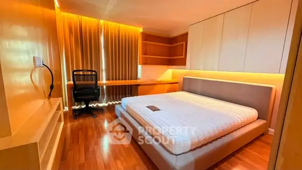 Modern bedroom with sleek design, featuring a large bed, built-in desk, and warm lighting.
