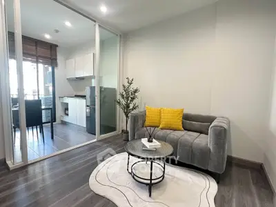 Modern living room with stylish gray sofa and open kitchen layout, featuring sleek appliances and bright decor.