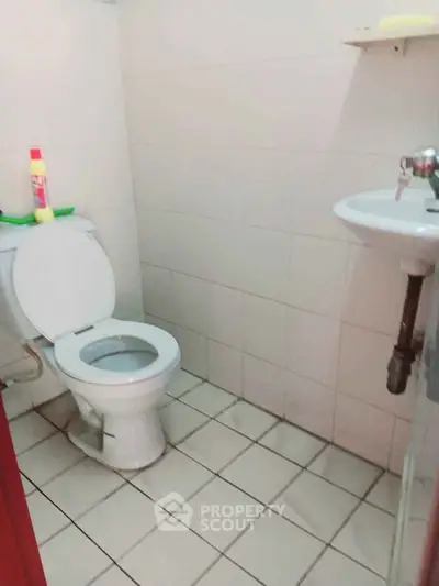 Compact bathroom with tiled floor, toilet, and wall-mounted sink.