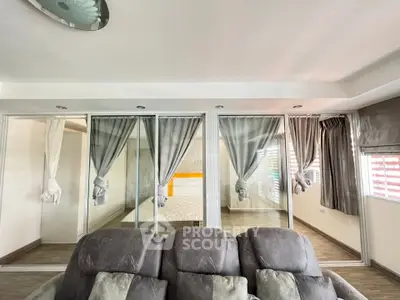 Spacious living room with modern decor and glass partitions leading to a cozy bedroom.