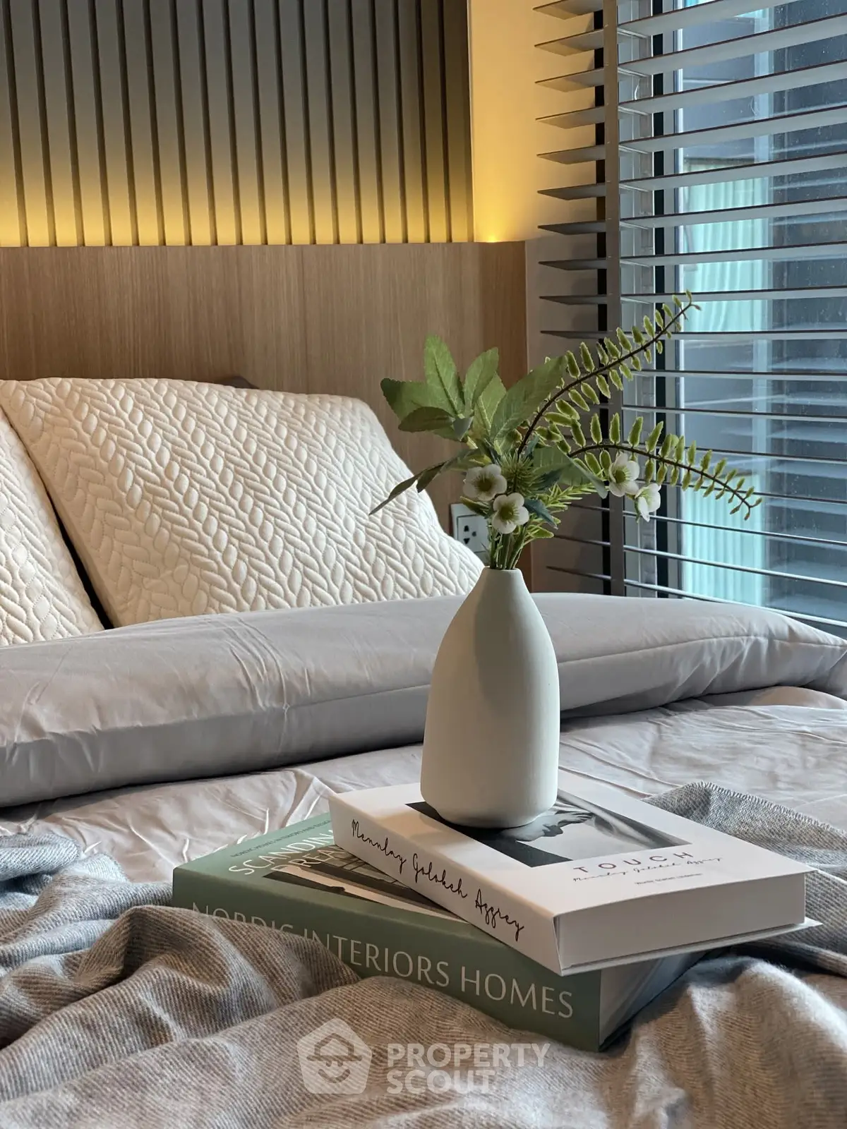 Cozy bedroom with stylish decor and natural light, featuring a vase with flowers on a bed.