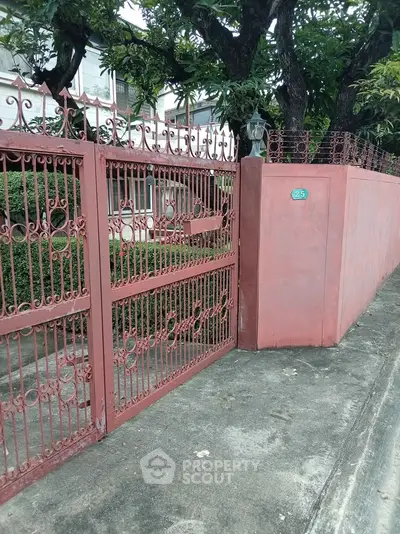 Charming red wrought iron gate with lush greenery in a serene neighborhood setting.