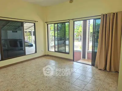 Spacious living room with large windows and tiled floor, offering abundant natural light and garden view.