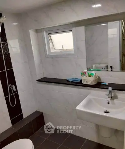 Modern bathroom with sleek white tiles and a large mirror, featuring a stylish sink and shower area.