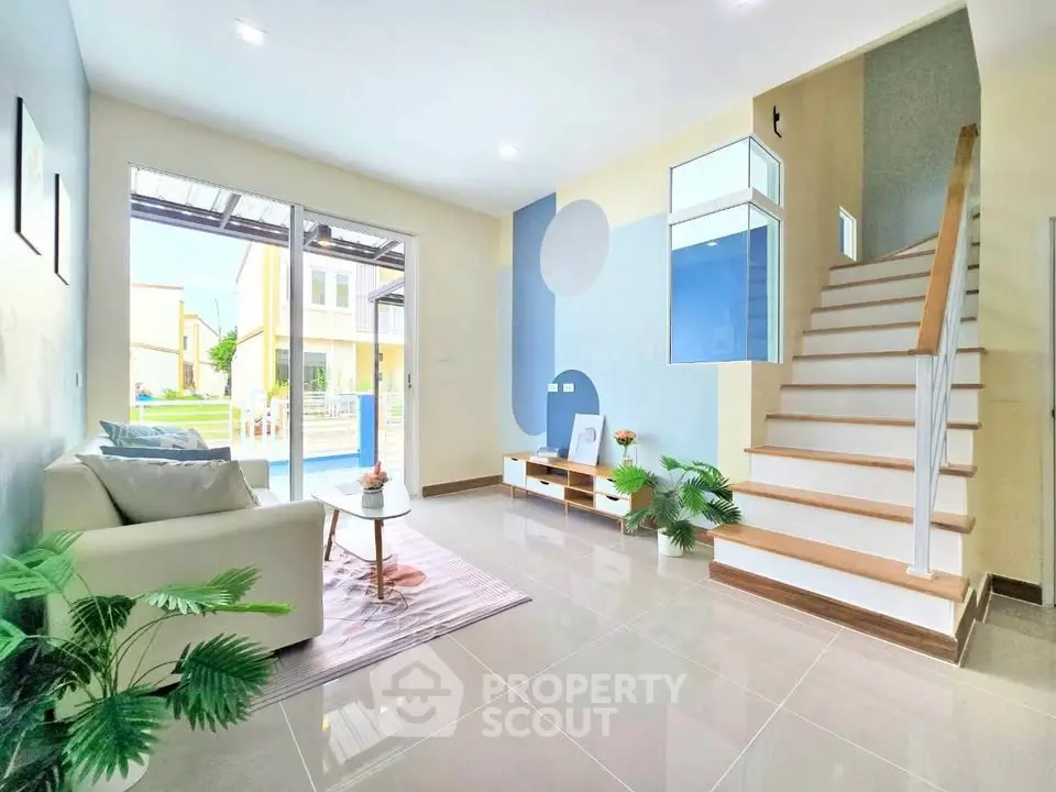 Modern living room with stylish decor and staircase, featuring large windows and natural light.