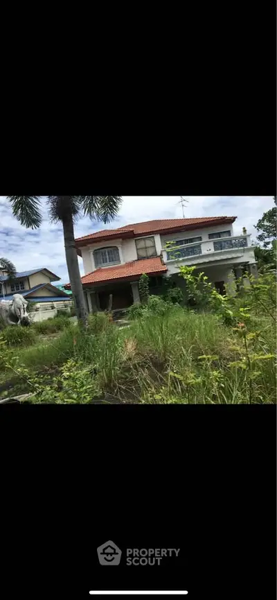 Charming two-story house with red-tiled roof and lush garden, perfect for serene living.