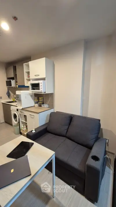 Modern compact living room with integrated kitchen featuring appliances and cozy seating area.