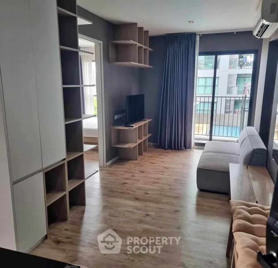 Modern living room with wooden flooring, stylish shelving, and a cozy sofa overlooking a balcony view.