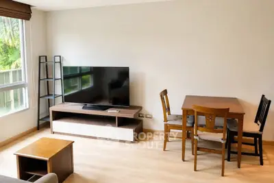 Modern living room with large TV and dining area, featuring natural light and stylish furniture.