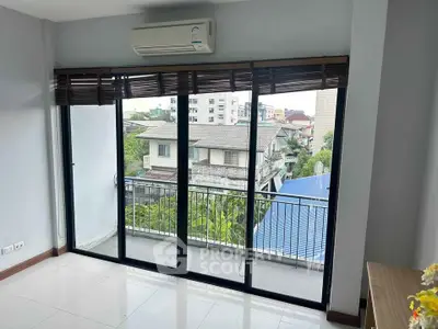 Spacious room with large windows and balcony offering a serene view of the neighborhood.