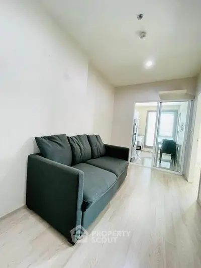 Modern living room with sleek sofa and wooden flooring, leading to a bright dining area.