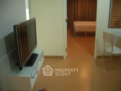 Modern apartment interior with TV, dining area, and view into bedroom.