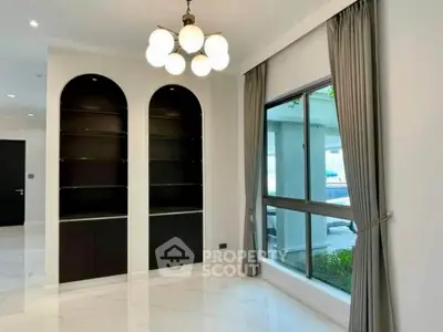 Elegant living room with modern chandelier and large window, featuring built-in shelves and stylish curtains.