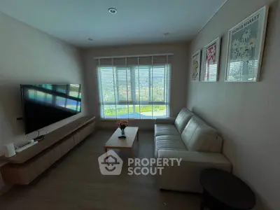 Modern living room with large TV and cozy seating area, featuring natural light and stylish decor.