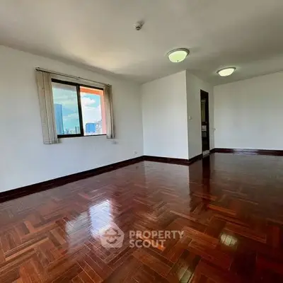 Spacious living room with polished wooden floors and large window offering city views.