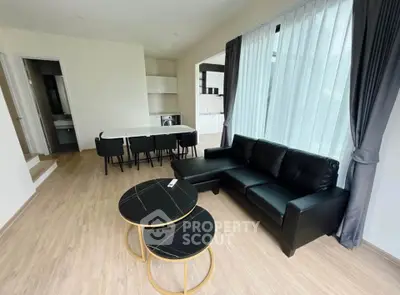 Modern living room with black leather sofa and stylish coffee tables, featuring open layout and natural light.