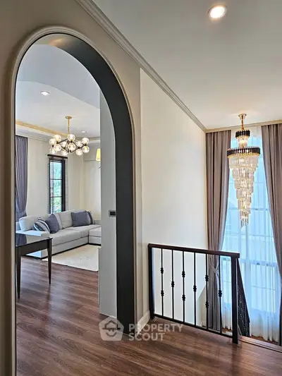 Elegant living room with modern decor and large windows, featuring a stylish chandelier and cozy seating area.