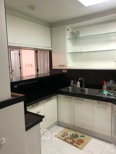 Modern kitchen with sleek black countertops and white cabinetry, featuring open shelving and a stainless steel sink.