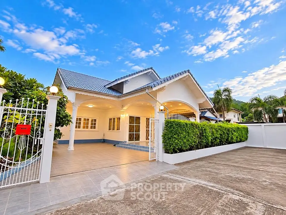Charming single-story house with spacious driveway and lush greenery under a vibrant blue sky.
