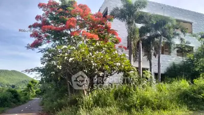 Stunning white building with lush greenery and vibrant red flowering tree, offering serene natural surroundings.