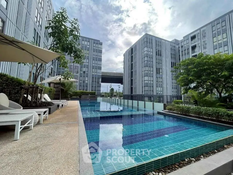 Modern apartment complex with a luxurious outdoor pool and sun loungers.