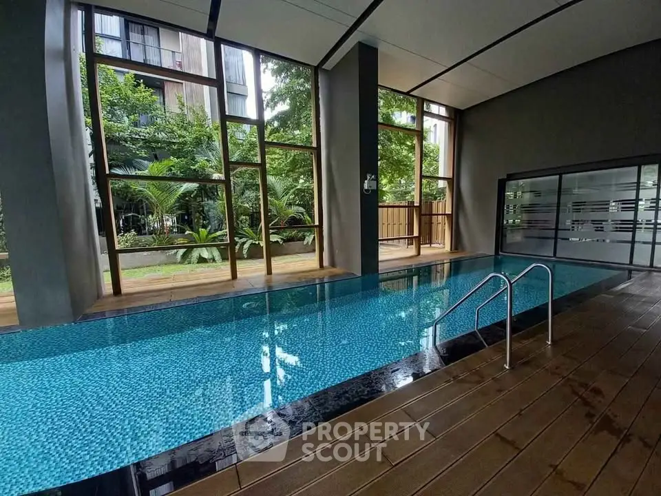 Luxurious indoor pool with floor-to-ceiling windows and lush garden view in modern building.