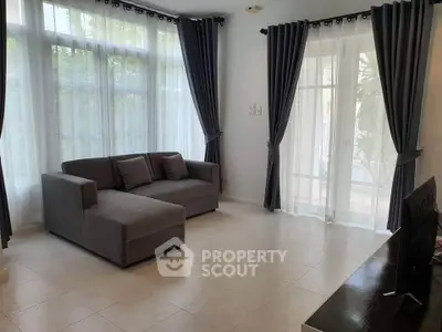 Spacious living room with modern gray sofa and large windows with elegant curtains.