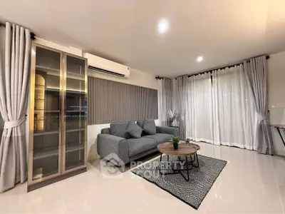 Modern living room with sleek gray sofa, glass cabinet, and elegant curtains in a stylish apartment.