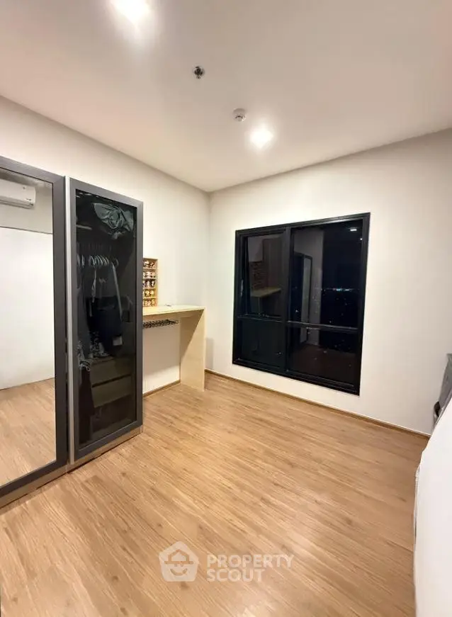 Spacious bedroom with wooden flooring and large window offering city views.