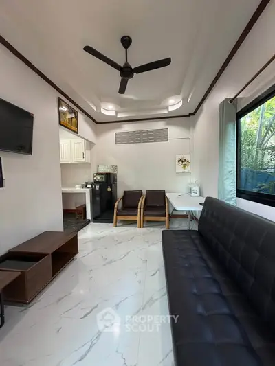 Modern living room with sleek furniture and natural light, featuring a ceiling fan and stylish decor.