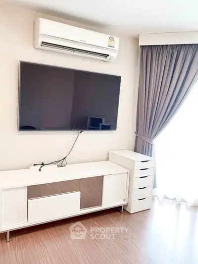 Modern living room with sleek TV setup and air conditioning, featuring elegant curtains and wooden flooring.