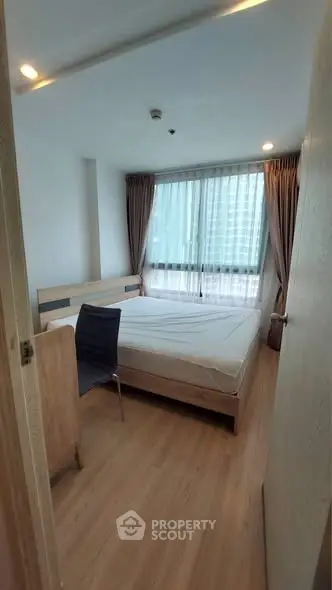 Modern bedroom with large window and wooden flooring in a high-rise apartment.