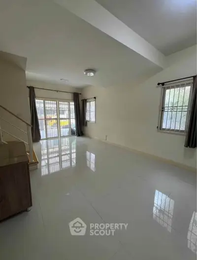 Spacious living room with large windows and glossy tiled floor, perfect for natural light and modern living.