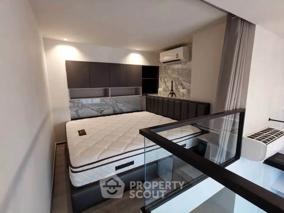 Modern bedroom with stylish decor and glass railing, featuring a comfortable bed and air conditioning unit.