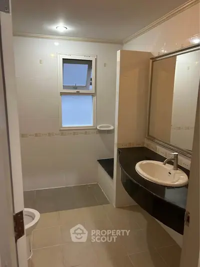 Spacious bathroom with modern sink and large mirror, featuring elegant tile design and natural light.
