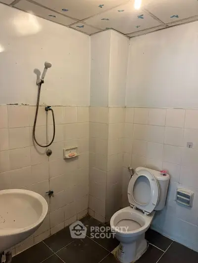 Basic bathroom with shower, sink, and toilet in a tiled setting.
