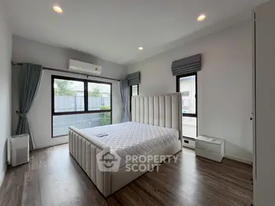 Spacious modern bedroom with large windows and elegant bed frame, featuring hardwood floors and natural light.