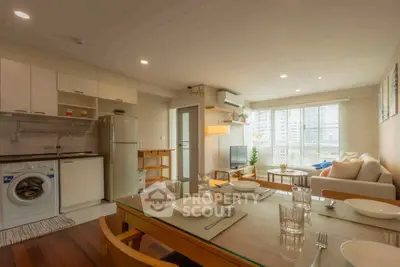 Modern open-plan living room with kitchen, featuring washing machine and cozy dining area.