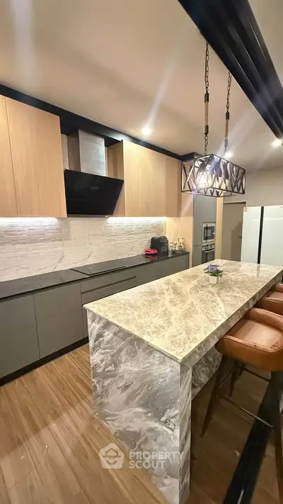 Modern kitchen with marble island and stylish lighting, featuring sleek cabinetry and integrated appliances.