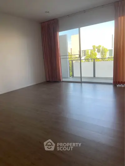 Spacious empty room with large window and wooden flooring, ideal for customization.