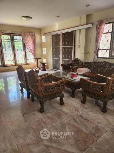 Spacious living room with elegant carved wooden furniture and large windows.