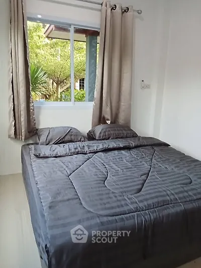 Cozy bedroom with large window and elegant curtains, offering a serene garden view.