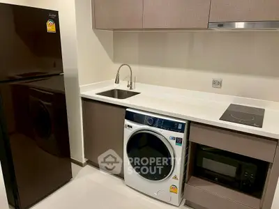Modern kitchen with sleek appliances including fridge, washing machine, and microwave in compact layout.
