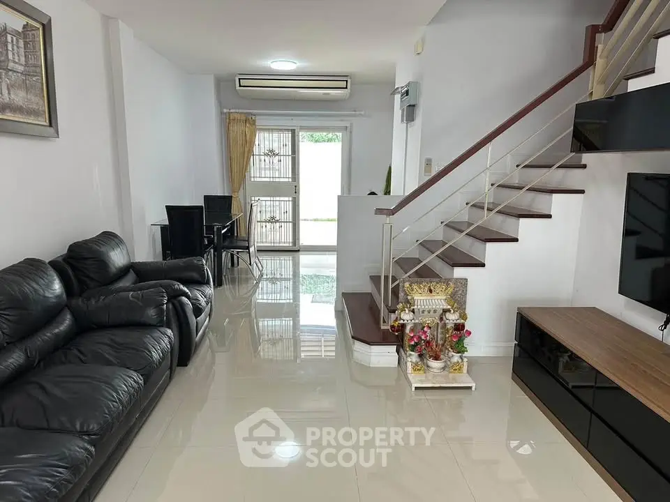 Spacious modern living room with sleek staircase and leather sofa, perfect for family gatherings.