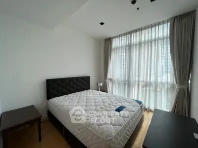 Spacious bedroom with large window and modern furnishings in a high-rise apartment.